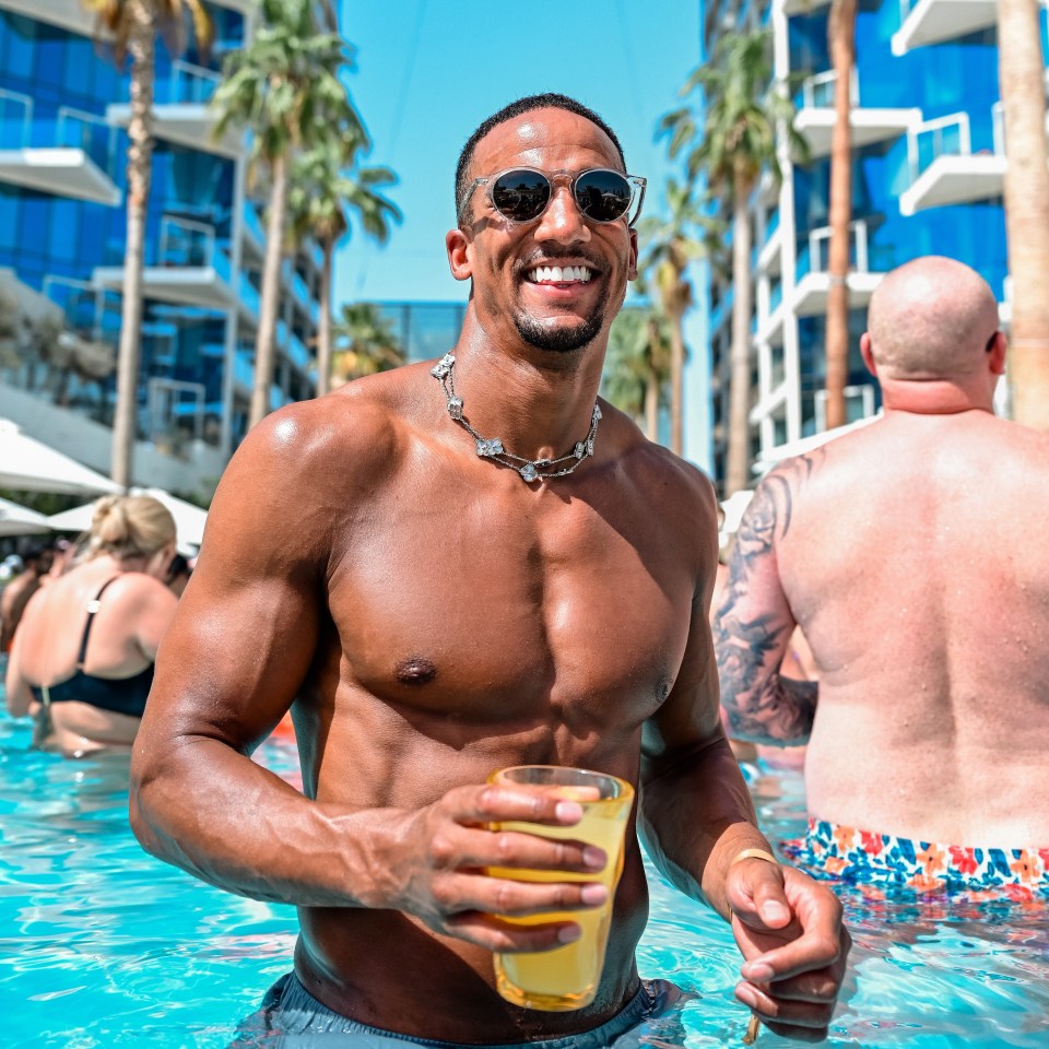 a shirtless man in a pool holding a glass of beer