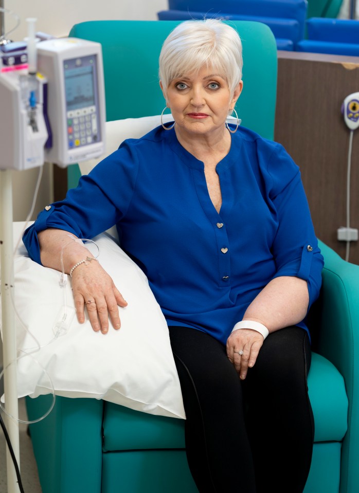 a woman in a blue shirt sits in a hospital chair