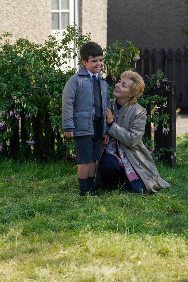 a woman kneeling down next to a boy in a grey jacket