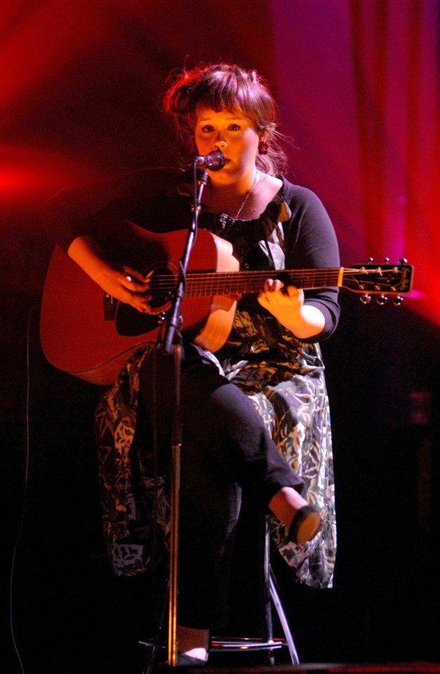 a woman singing into a microphone while holding a guitar