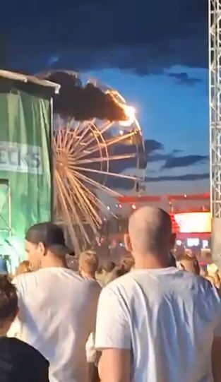 One of the compartments on the ferris wheel burns as people look on from the festival crowd