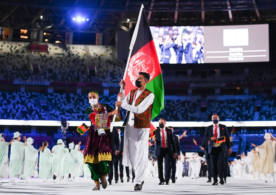 a man holding a flag in front of a screen that says tokyo 2020