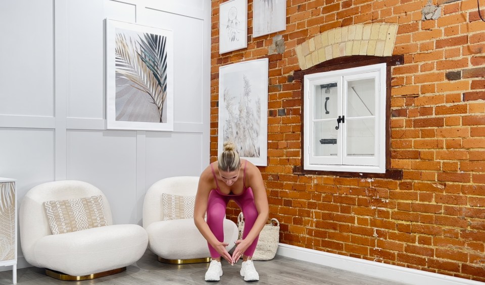 a woman stretches her legs in front of a brick wall