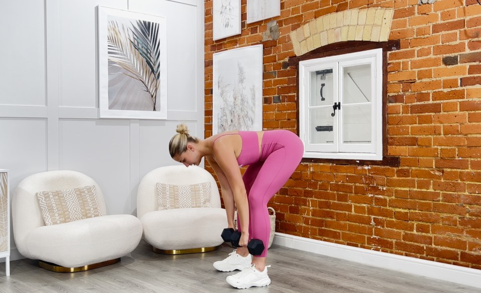 a woman lifting a dumbbell in front of a brick wall