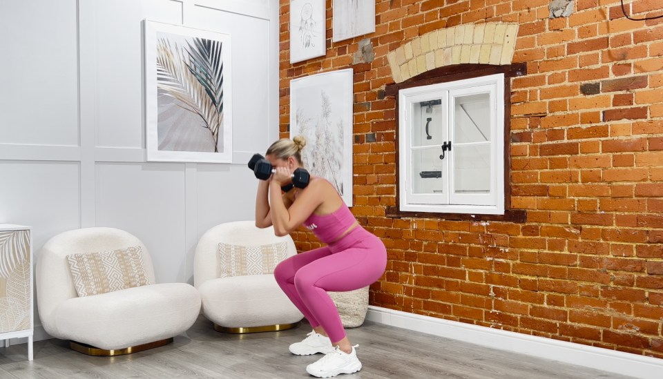 a woman squatting with dumbbells in front of a brick wall