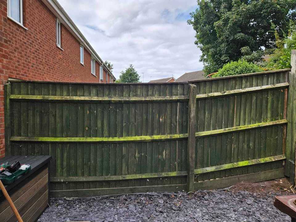 a green fence with a brick building in the background