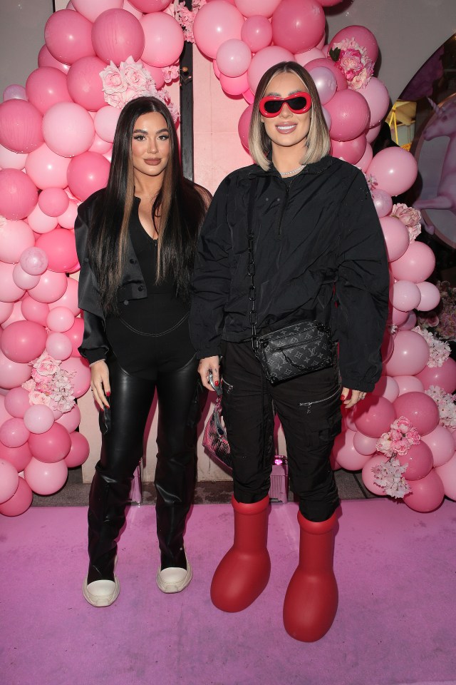 two women standing in front of a wall of pink balloons