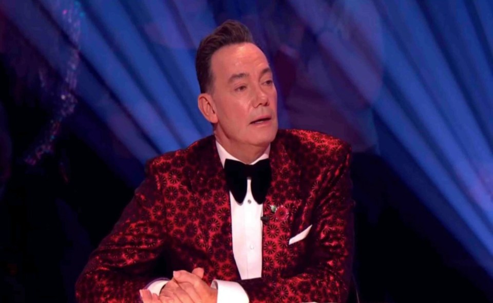 a man in a red tuxedo and bow tie is sitting with his hands folded