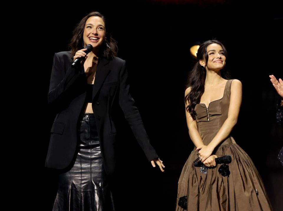 a woman in a black jacket stands next to another woman in a brown dress