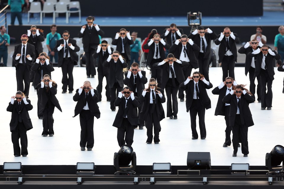 a group of men in suits and sunglasses are dancing on a stage