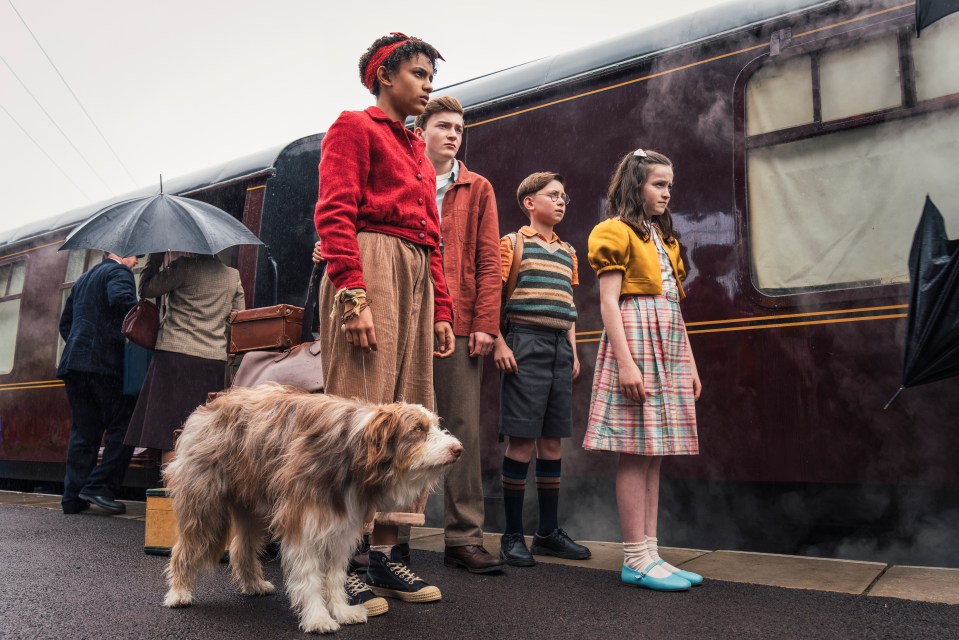 a group of children and a dog are standing in front of a train