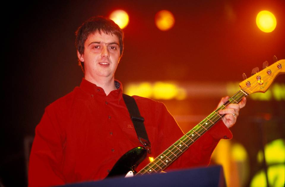 a man in a red shirt is playing a fender bass guitar