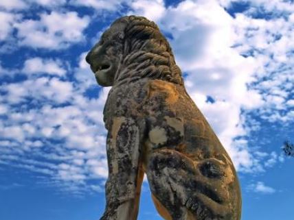 a statue of a lion is sitting in front of a blue sky with clouds .