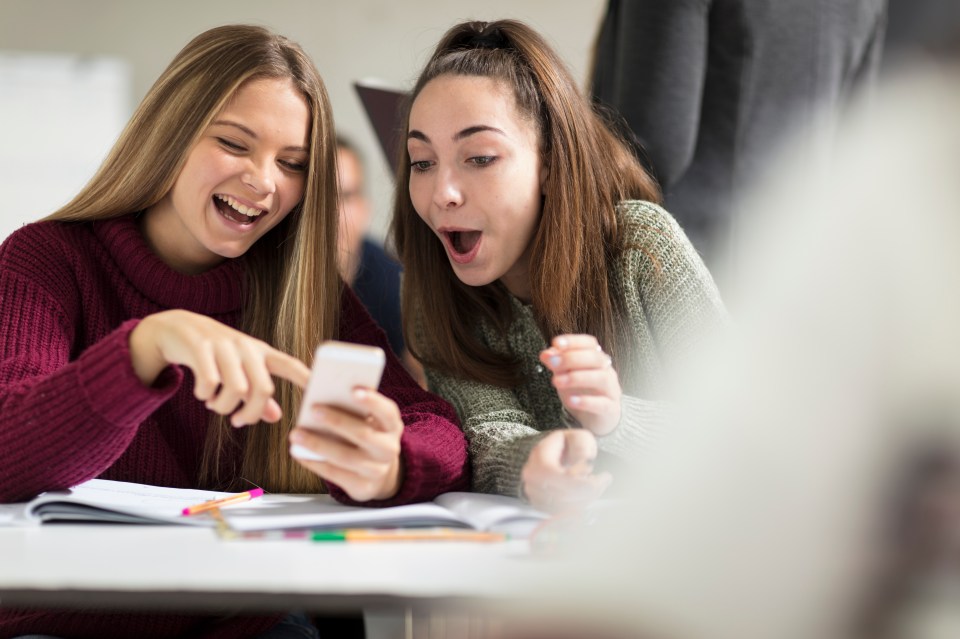 two girls are laughing while looking at a cell phone