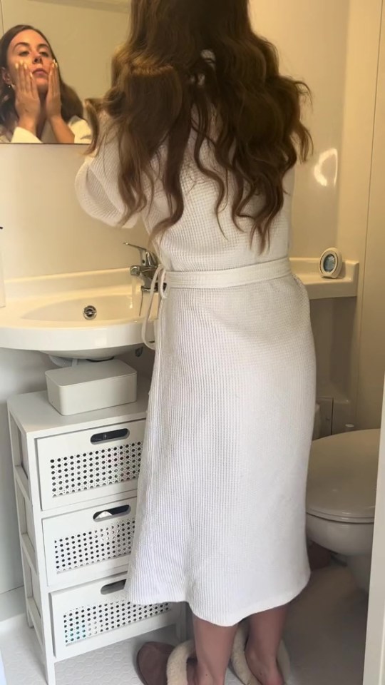 a woman in a white robe is standing in front of a bathroom sink