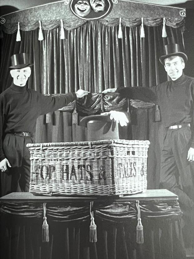 two men standing next to a basket that says top hats & this