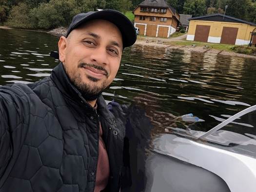 a man is taking a selfie in front of a boat on a lake .