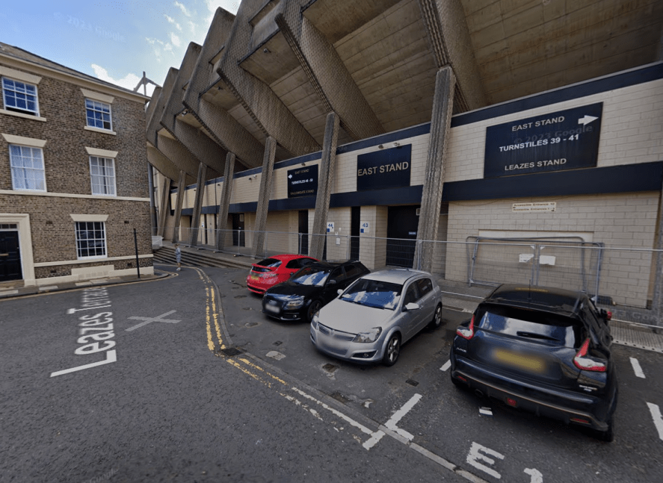 cars are parked in front of a building that says east stand