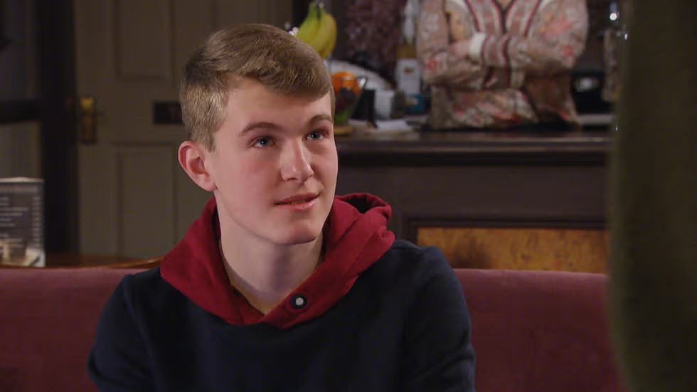 a young man in a red hoodie sits on a couch