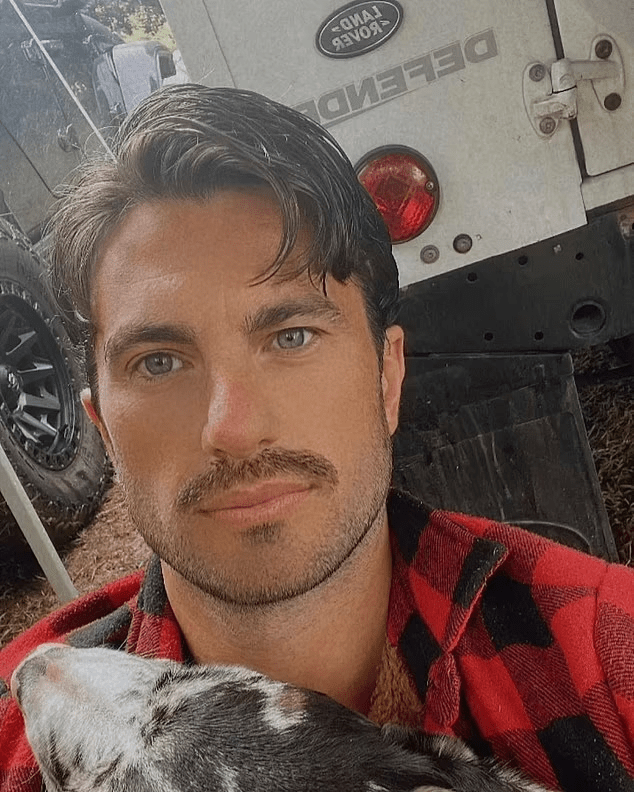 a man holding a dog in front of a land rover defender