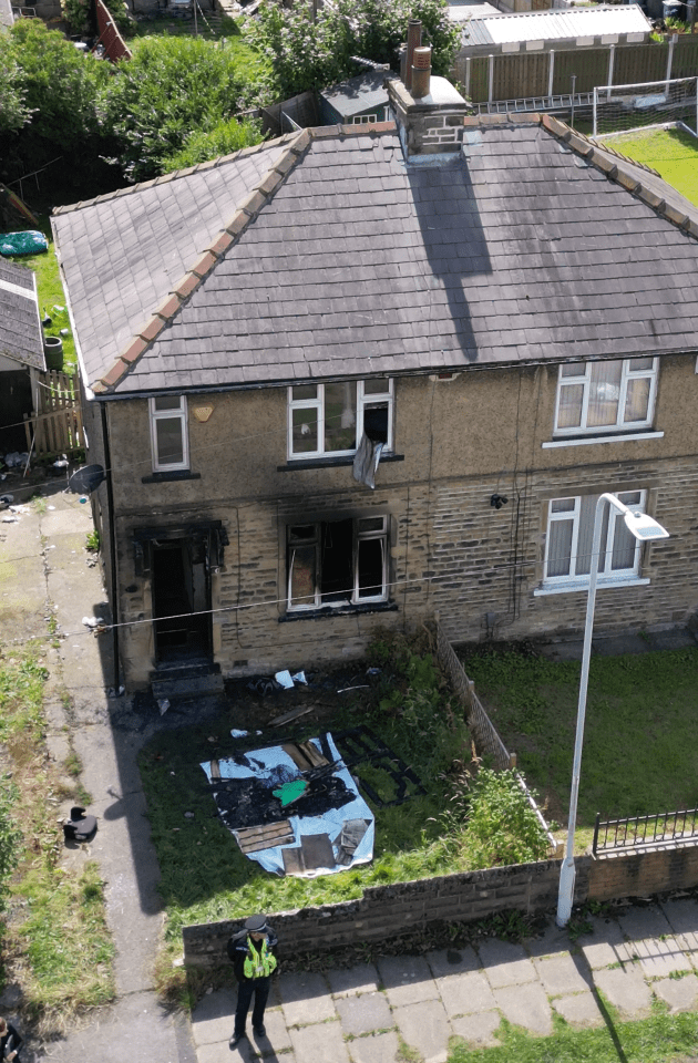 a police officer stands in front of a house that has been damaged by fire