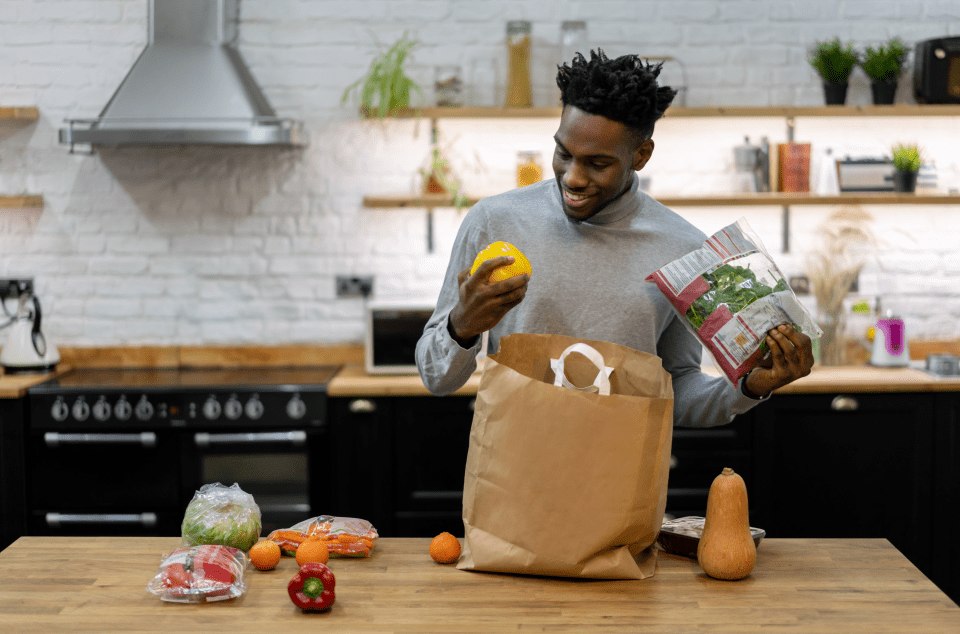 a man is holding a bag of salad and a yellow pepper