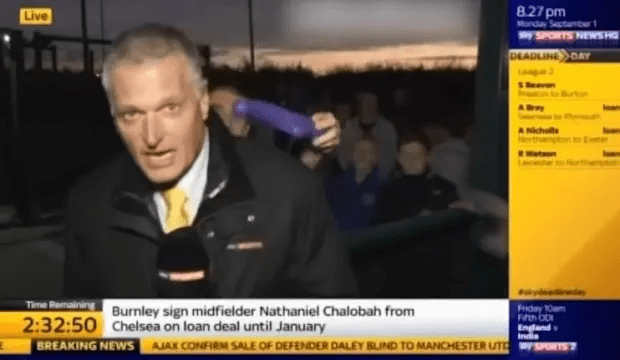 a man is holding a purple object in front of a screen that says breaking news