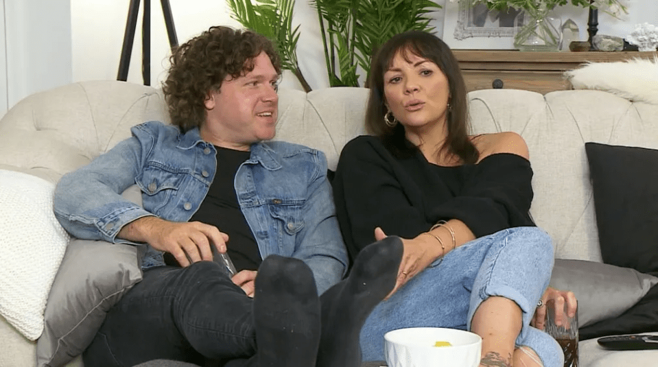 a man and a woman sit on a couch with their feet up