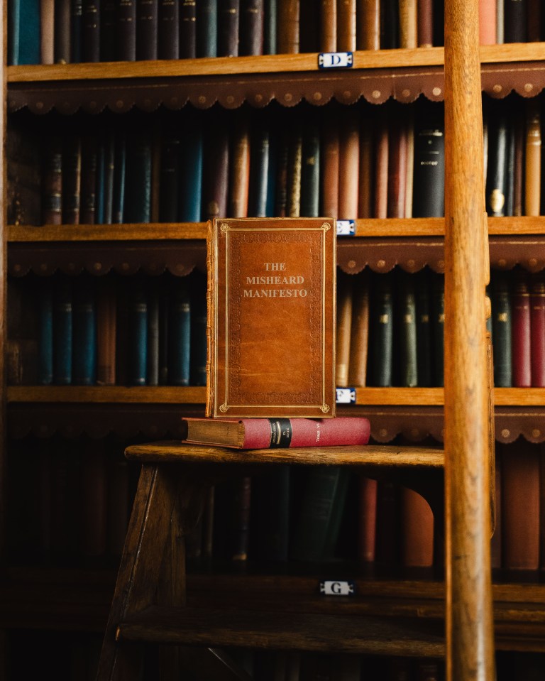 a book titled the misheard manifesto sits on a wooden shelf