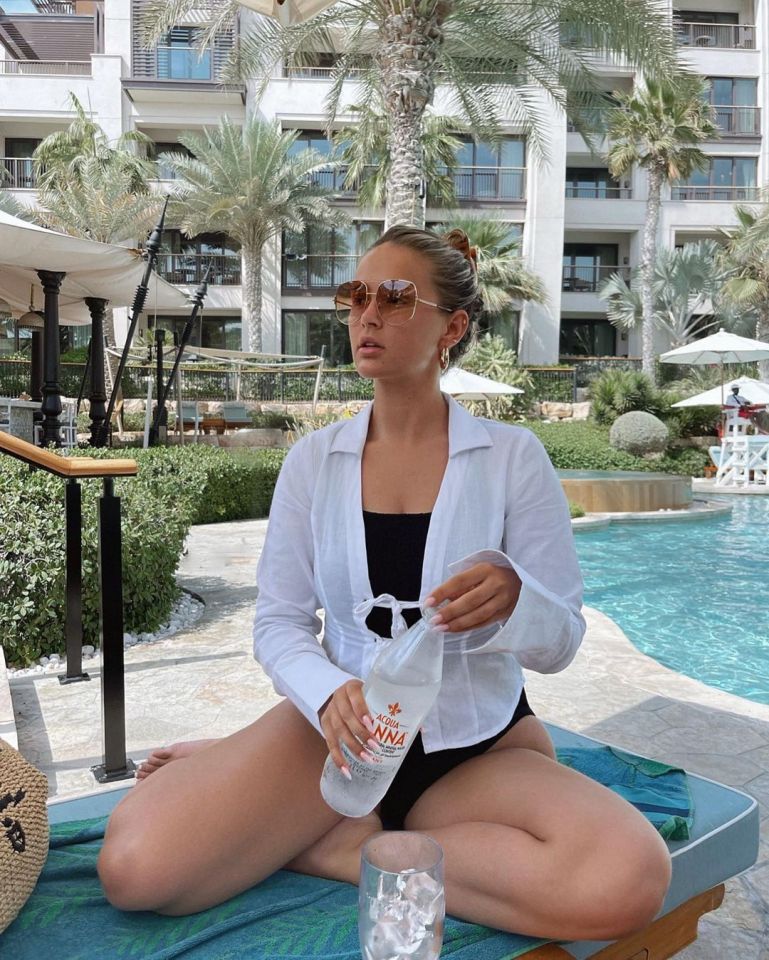 a woman in a bathing suit sits by a pool holding a bottle of anna water