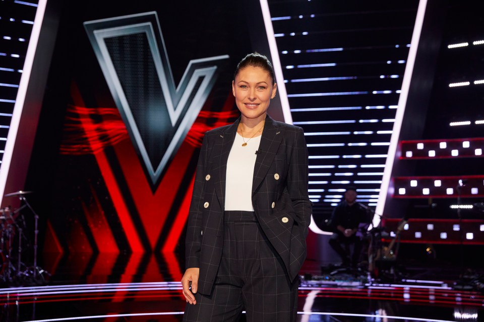 a woman in a suit stands in front of a large v on a stage