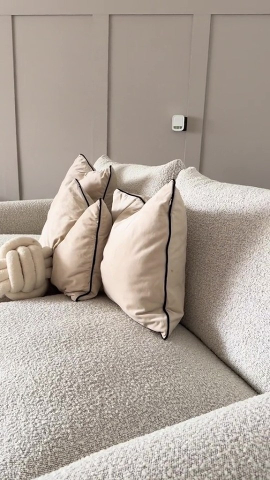 a couch with pillows and a thermostat on the wall