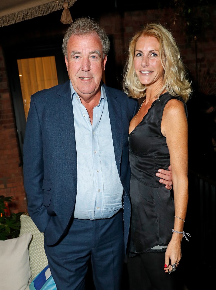 a man in a suit stands next to a woman in a black tank top