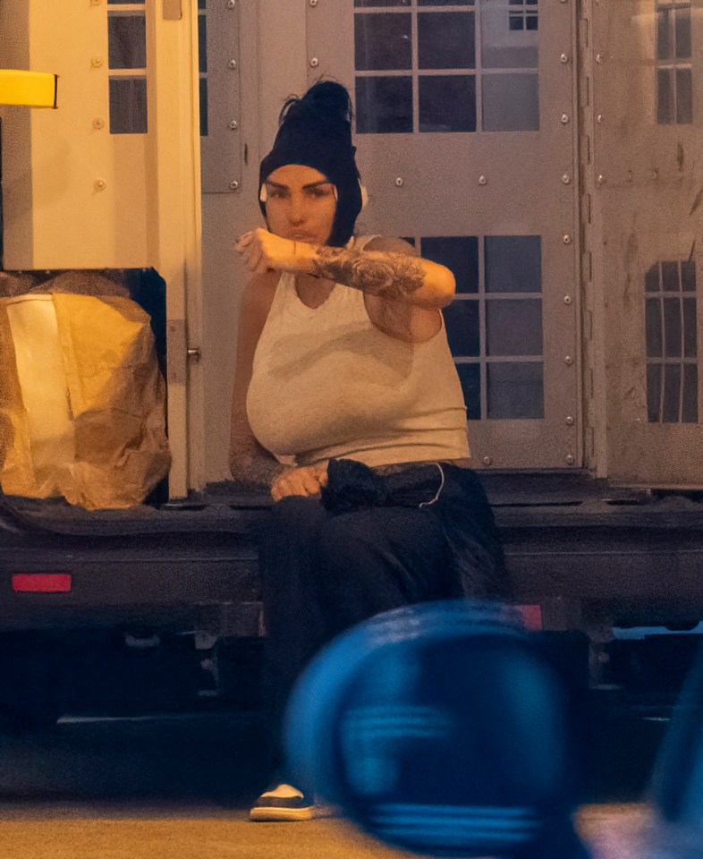 a woman wearing a black beanie and a white tank top sits on the back of a truck