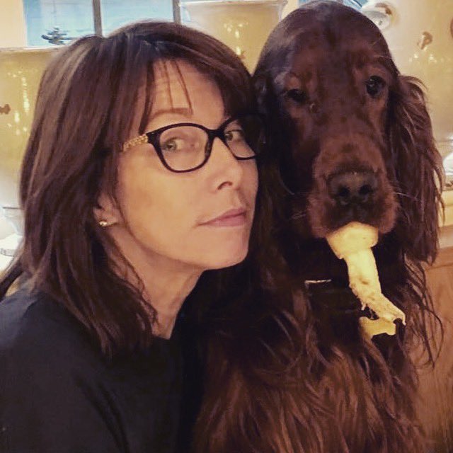 a woman wearing glasses is standing next to a dog with a stick in its mouth .