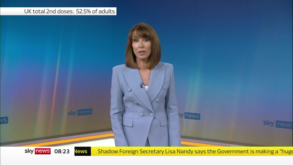 a woman stands in front of a sky news screen