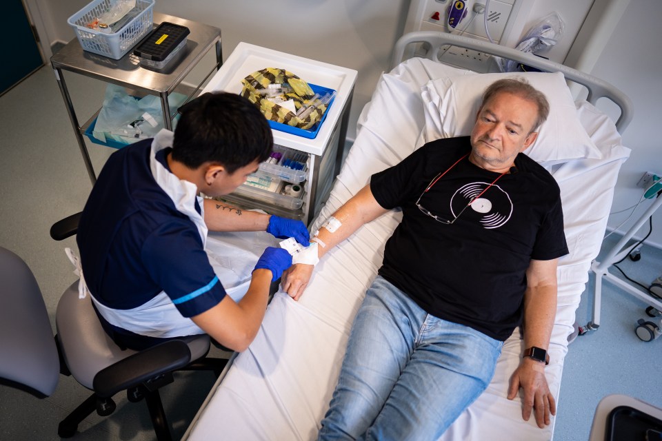 a man in a black shirt with a record on it is laying in a hospital bed