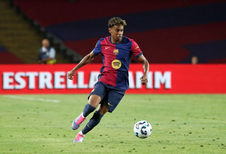 a soccer player dribbles a ball in front of an estrella damm sign