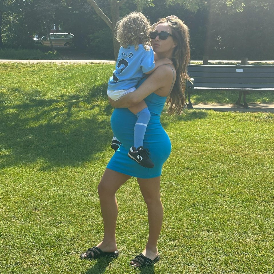 a pregnant woman in a blue dress is holding a baby in a blue shirt that says dad