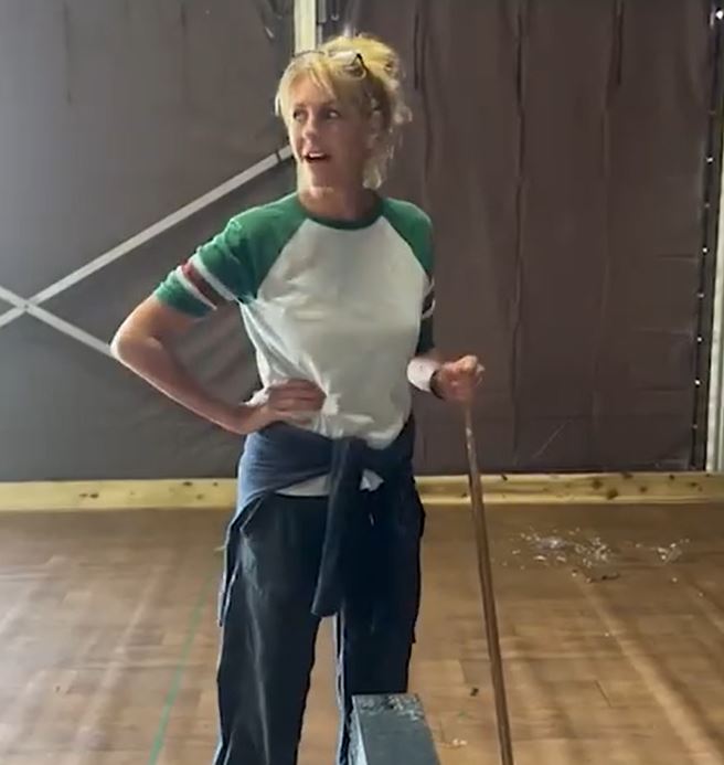 a woman is standing on a wooden floor holding a mop .