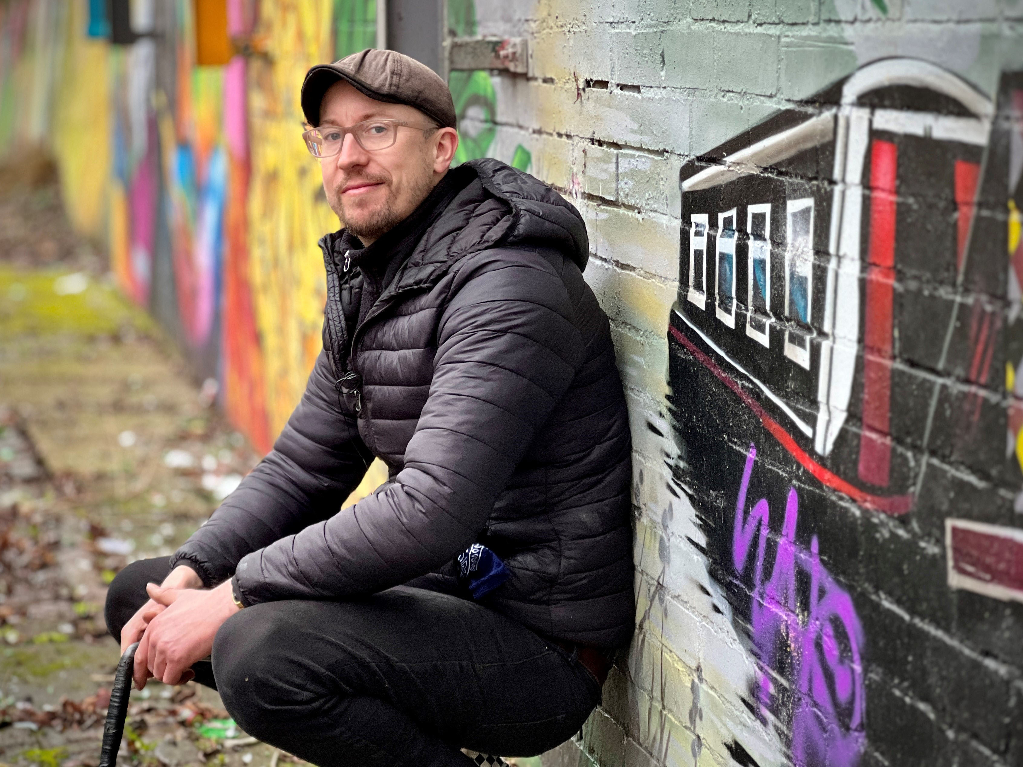 a man leans against a brick wall with graffiti on it