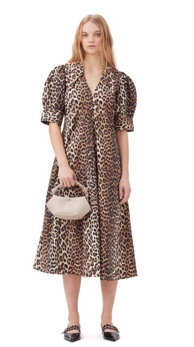 a woman is wearing a leopard print dress and holding a white bag .