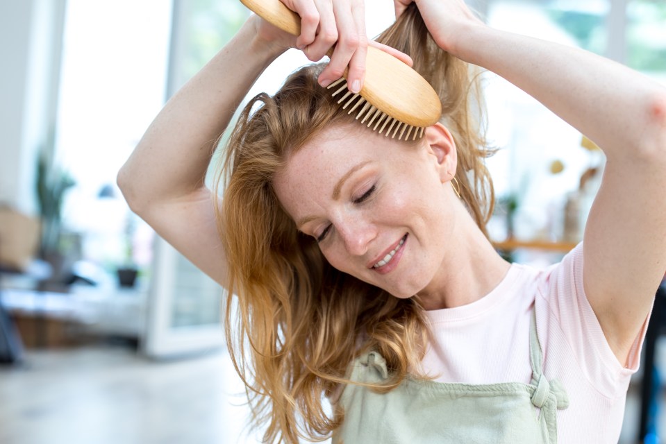 a woman brushing her hair with a wooden brush