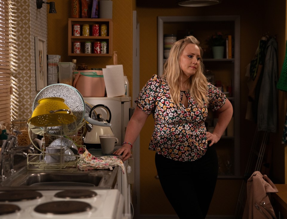 a woman in a floral shirt stands in a kitchen