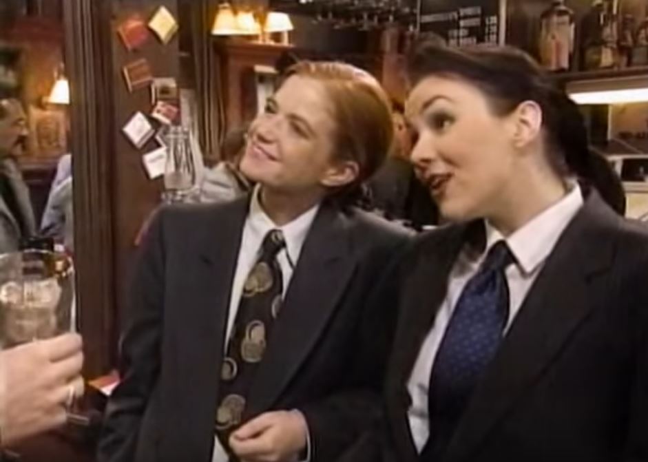 two women in suits and ties are standing next to each other in a bar .