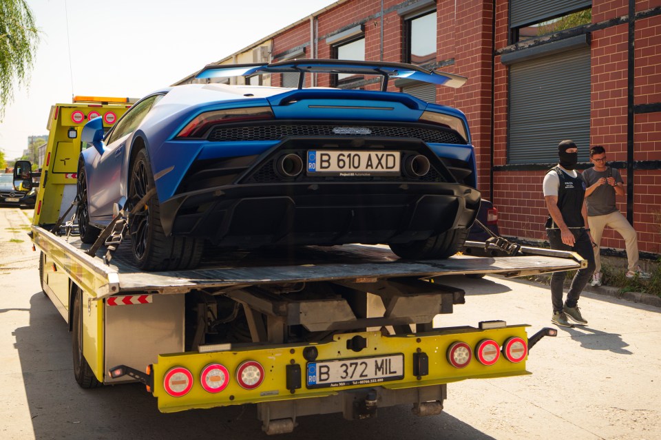 A masked police officer walks as a Lamborghini Huracan is removed by authorities from Andrew Tate’s residence on the outskirts of Bucharest