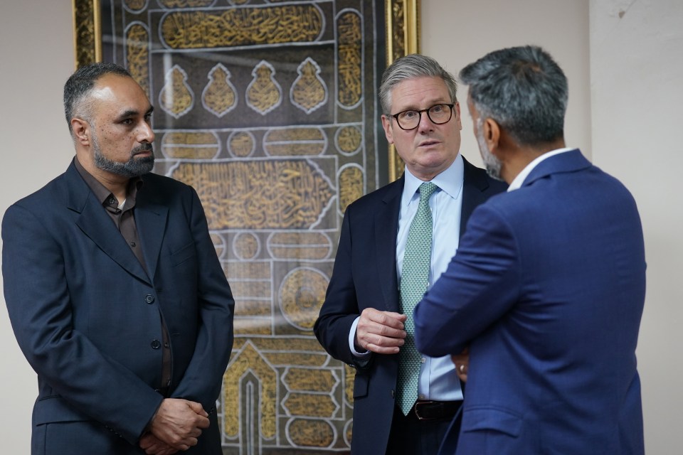 three men are standing in front of a painting with arabic writing on it