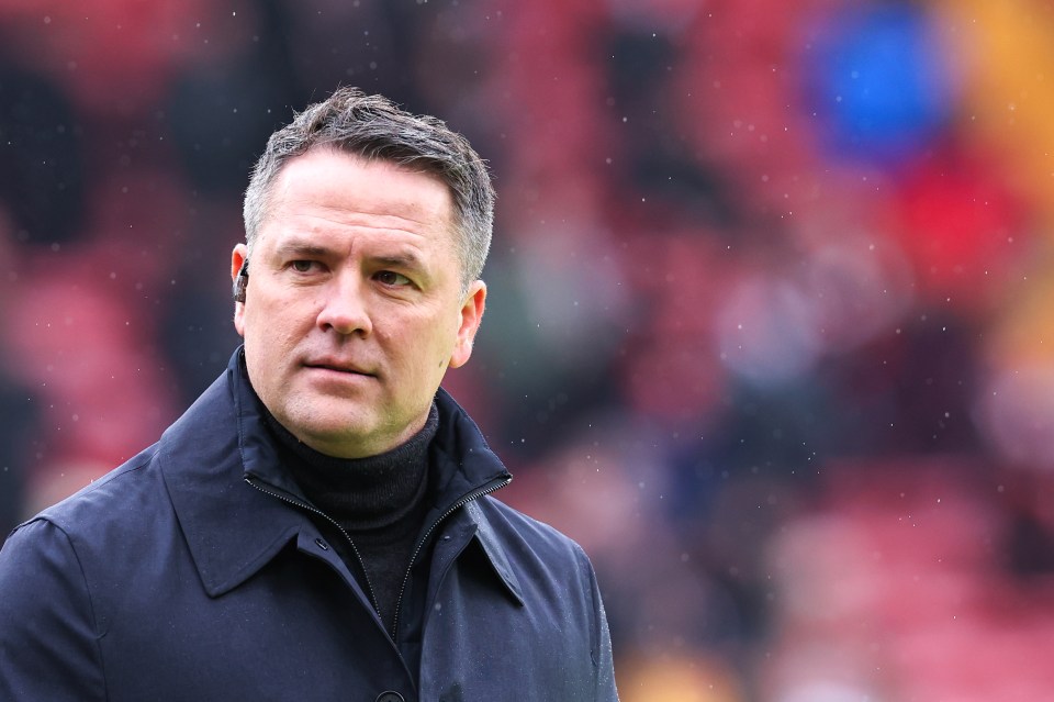 a man in a black coat stands on a soccer field