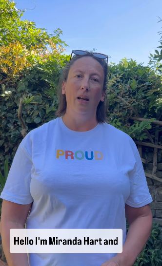 a woman wearing a white t-shirt with the word proud on it is standing in front of a bush .