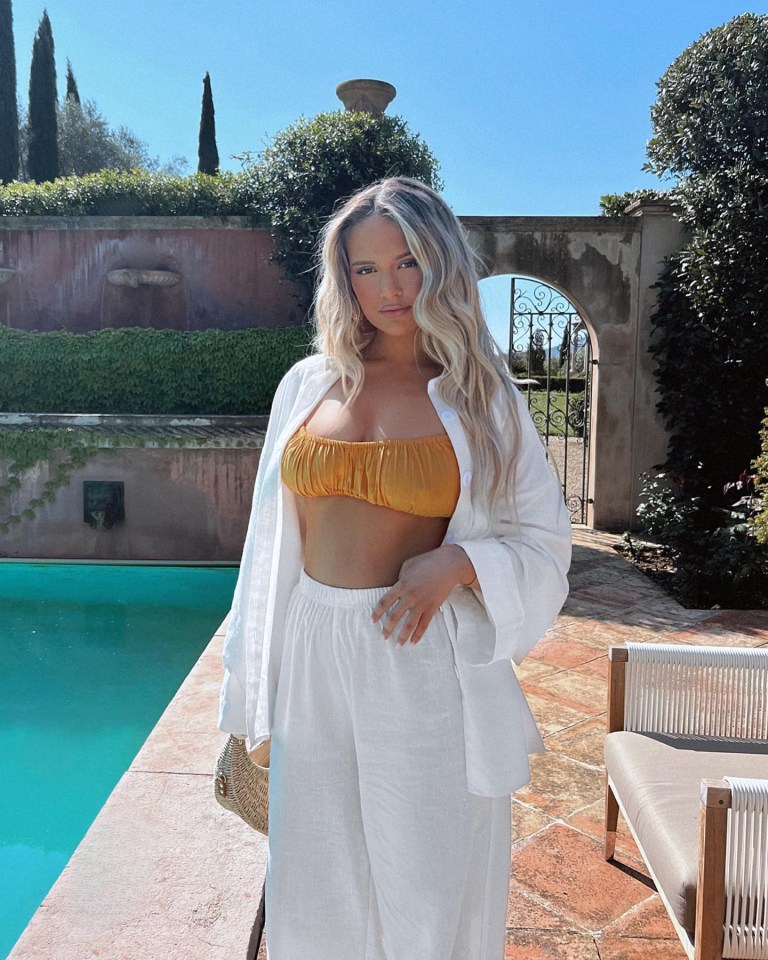 a woman in a bikini top and white pants stands next to a pool